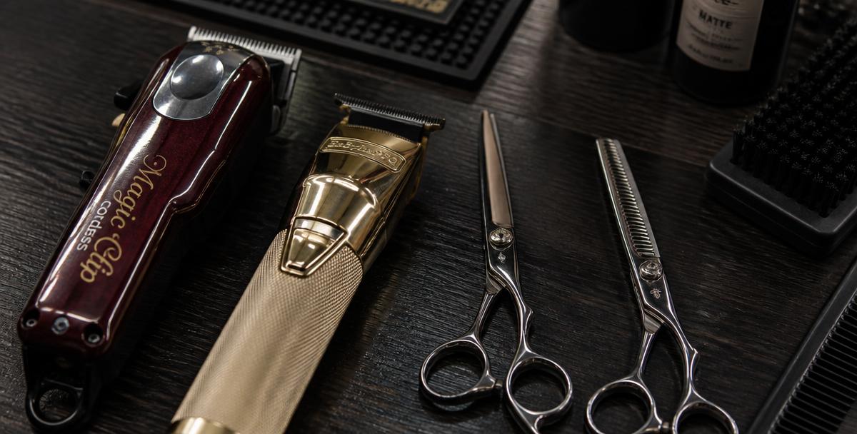 Close up of barber tools, clippers, and scissors on a dark wood station